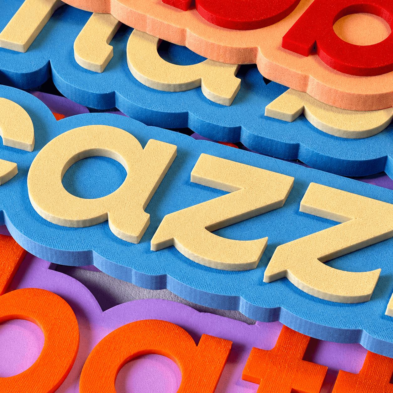 Close-up of Notami lettering 3D printed in PLA: raised cream letters on light blue and peach bases, on top of more orange and purple lettering