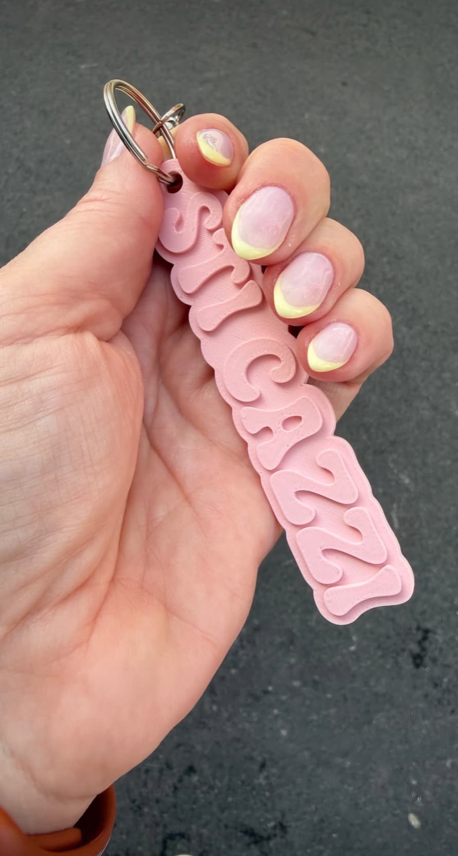 Manicured hand holding the pink keychain reading “STICAZZI”